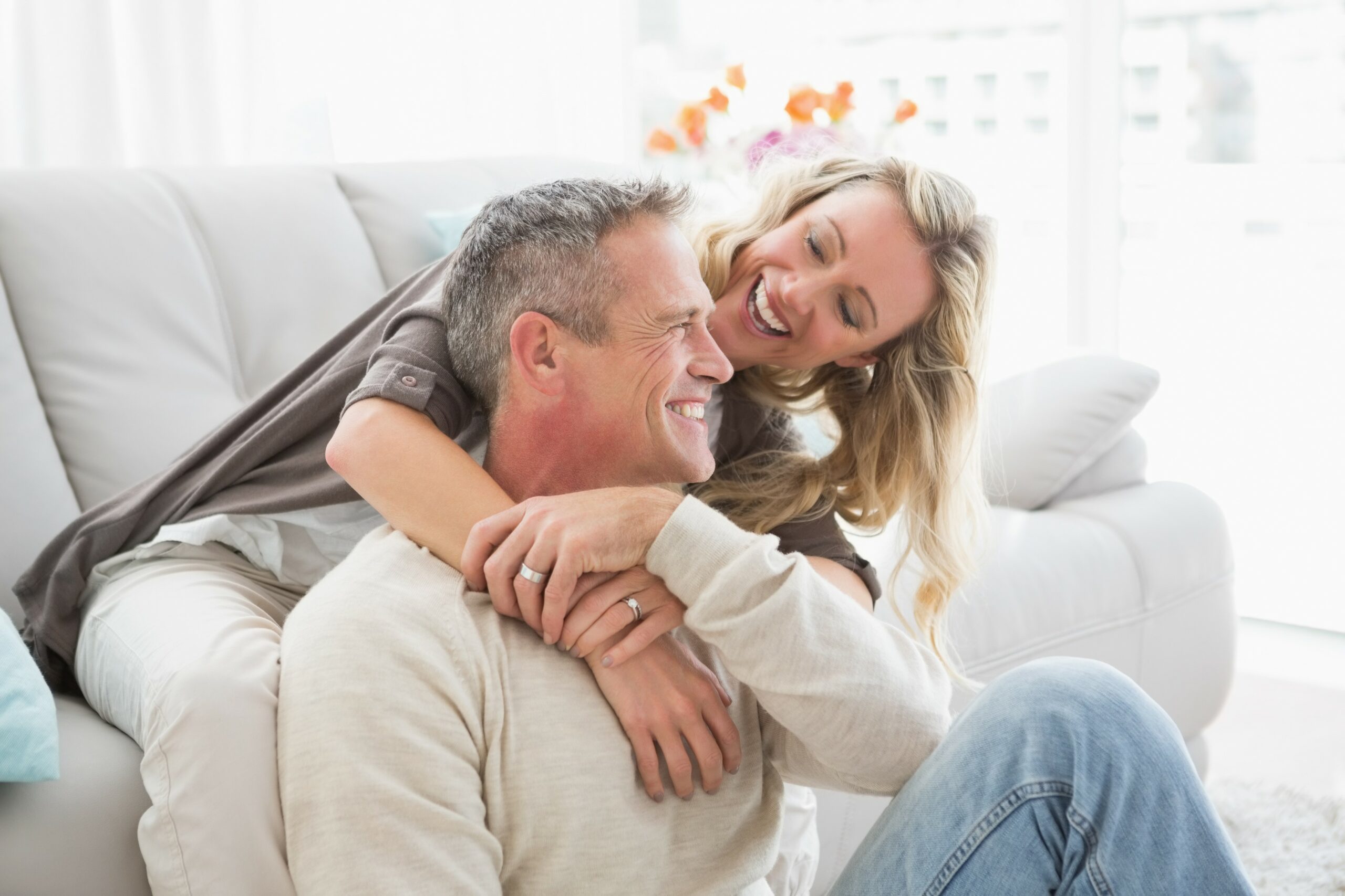 emotionale_intimität älteres Pärchen kuschelt an einer Couch und blickt sich lächelnd an - die emotionale Intimität ist spürbar