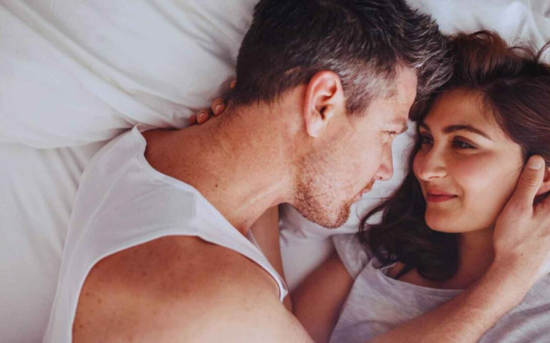 Liebespaar liegt im Bett und sieht sich verliebt an - sie leben die 5 Regeln für eine glückliche Beziehung