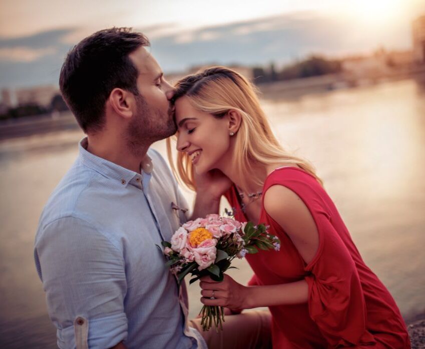 Präsenzseminar_Kuss_Stirn Mann küsst Frau auf Stirn und sie hält Blumen von ihm in der Hand, so entfacht man Liebe neu